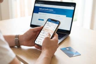 Hands hold a smartphone displaying a banking app with 'AMZ Digital FRA' highlighted. A credit card and laptop showing 'Refund Confirmation' are on a desk.