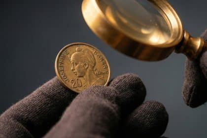 A gloved hand carefully holds a 20 centimes Joséphine Baker coin, examined by a vintage magnifying glass on a blurred charcoal background.