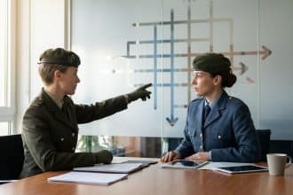 Two uniformed officers discuss career progression in a modern office. One points to a blurred chart symbolizing advancement.