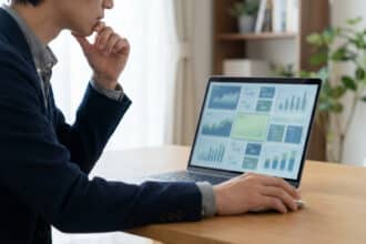 Homme pensif analysant des graphiques de données financières sur un laptop, main sur le menton, souris en main.