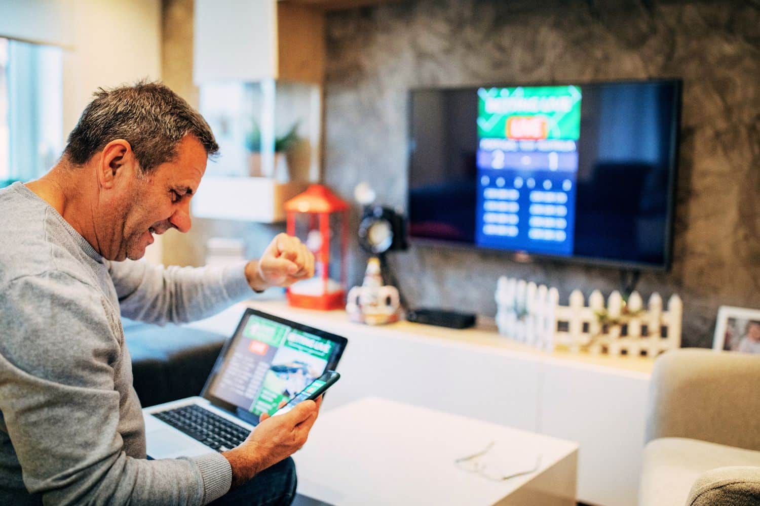 Homme célébrant victoire devant écran et smartphone