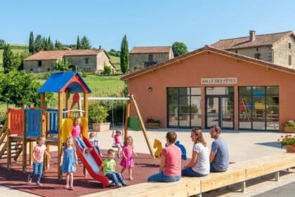 Enfants jouant dans une aire de jeux devant une salle des fêtes en zone rurale